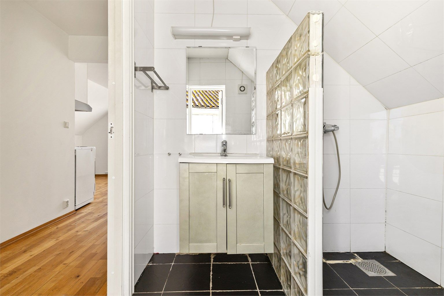Badet har flislagt gulv, dusjhjørne og servantinnredning.