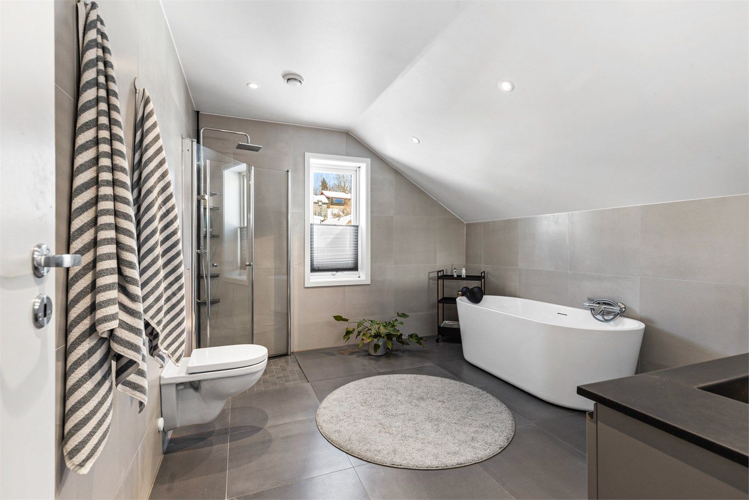 Badet i loftsetasjen har flislagt gulv med gulvvarme. Nedsenket himling med downlights. Vegghengt servantinnredning. Dobbel ovenpåliggende servant med armaturer.