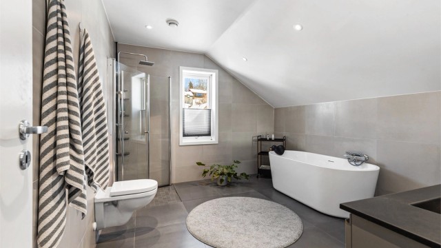 Badet i loftsetasjen har flislagt gulv med gulvvarme. Nedsenket himling med downlights. Vegghengt servantinnredning. Dobbel ovenpåliggende servant med armaturer.
