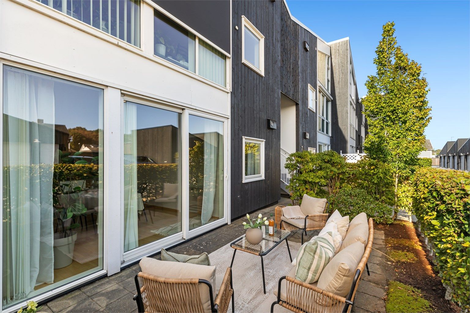 Terrassen strekker seg langs leilighetens fasade med store skyvedører inn til stuen.