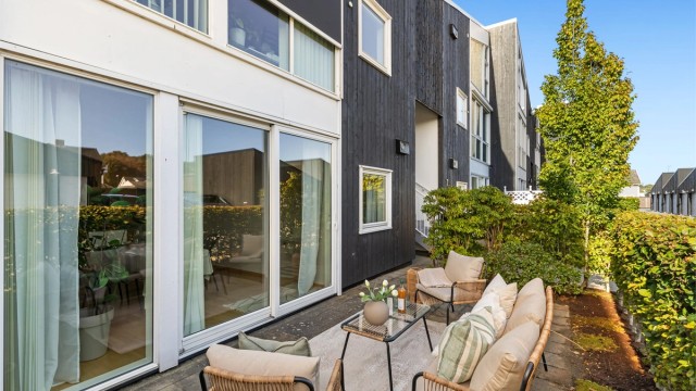 Terrassen strekker seg langs leilighetens fasade med store skyvedører inn til stuen.