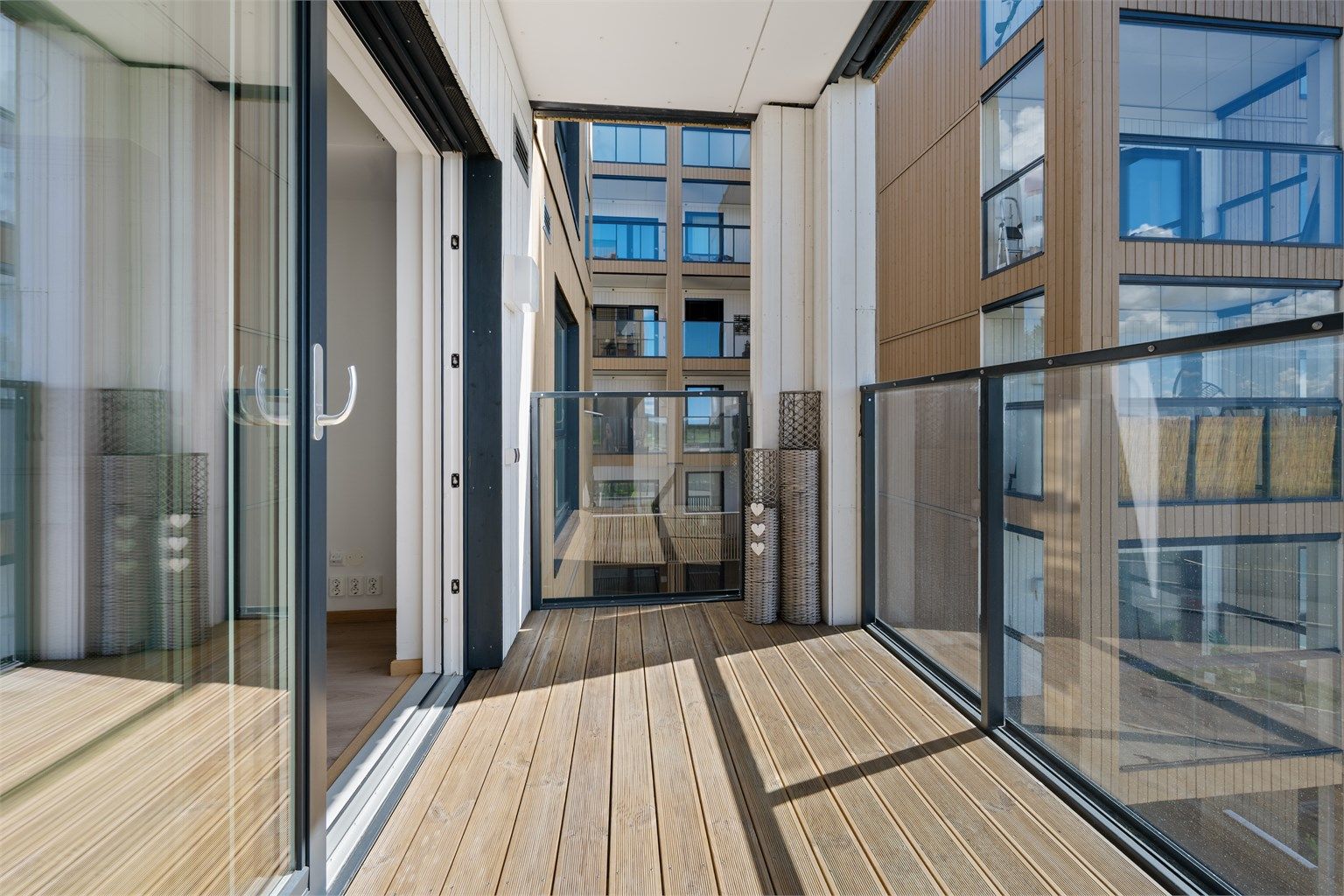 Den sørvendte balkongen har gulv belagt med terrassebord og rekkverk i glass og metall.