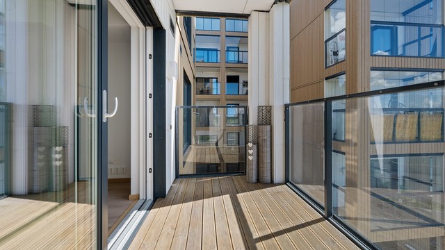 Den sørvendte balkongen har gulv belagt med terrassebord og rekkverk i glass og metall.