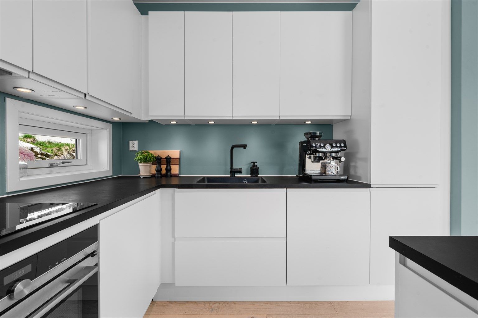 Moderne innredning med slette, hvite fronter og mørk benkeplate. Downlights gir godt arbeidslys.