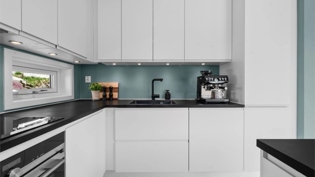 Moderne innredning med slette, hvite fronter og mørk benkeplate. Downlights gir godt arbeidslys.