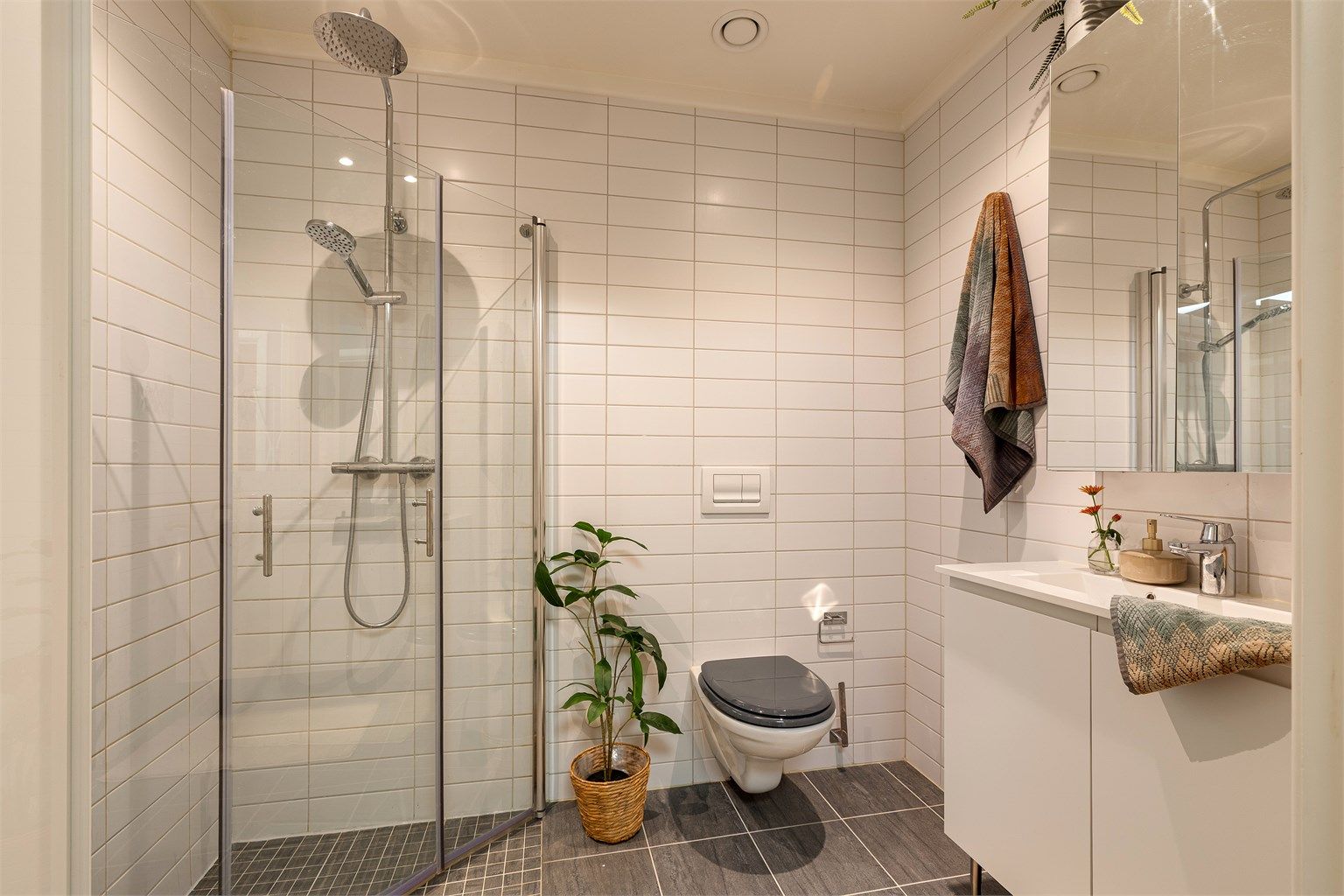 Badet i hovedetasjen har også vegghengt toalett, innfellbare glassdører i dusjen, og servant med speilskap over samt skap under. Downlights i himling.