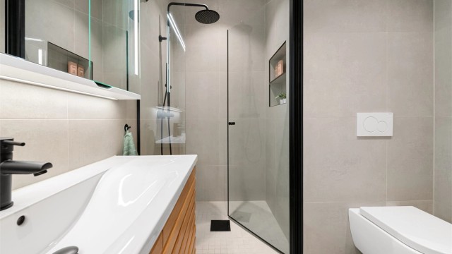 Badet er utstyrt med vegghengt toalett og dusjhjørne med innfellbare glassdører.