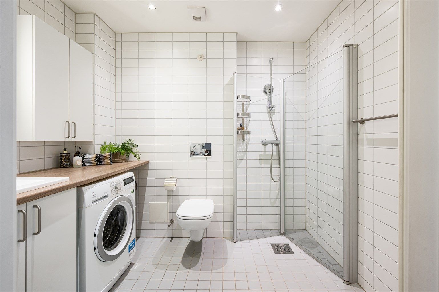 Lyst og delikat flislagt bad med gulvvarme og downlights. Badet består av benkeplate med servant, speil med belysning, vegghengt toalett og dusjhjørne med svingbare glassdører.