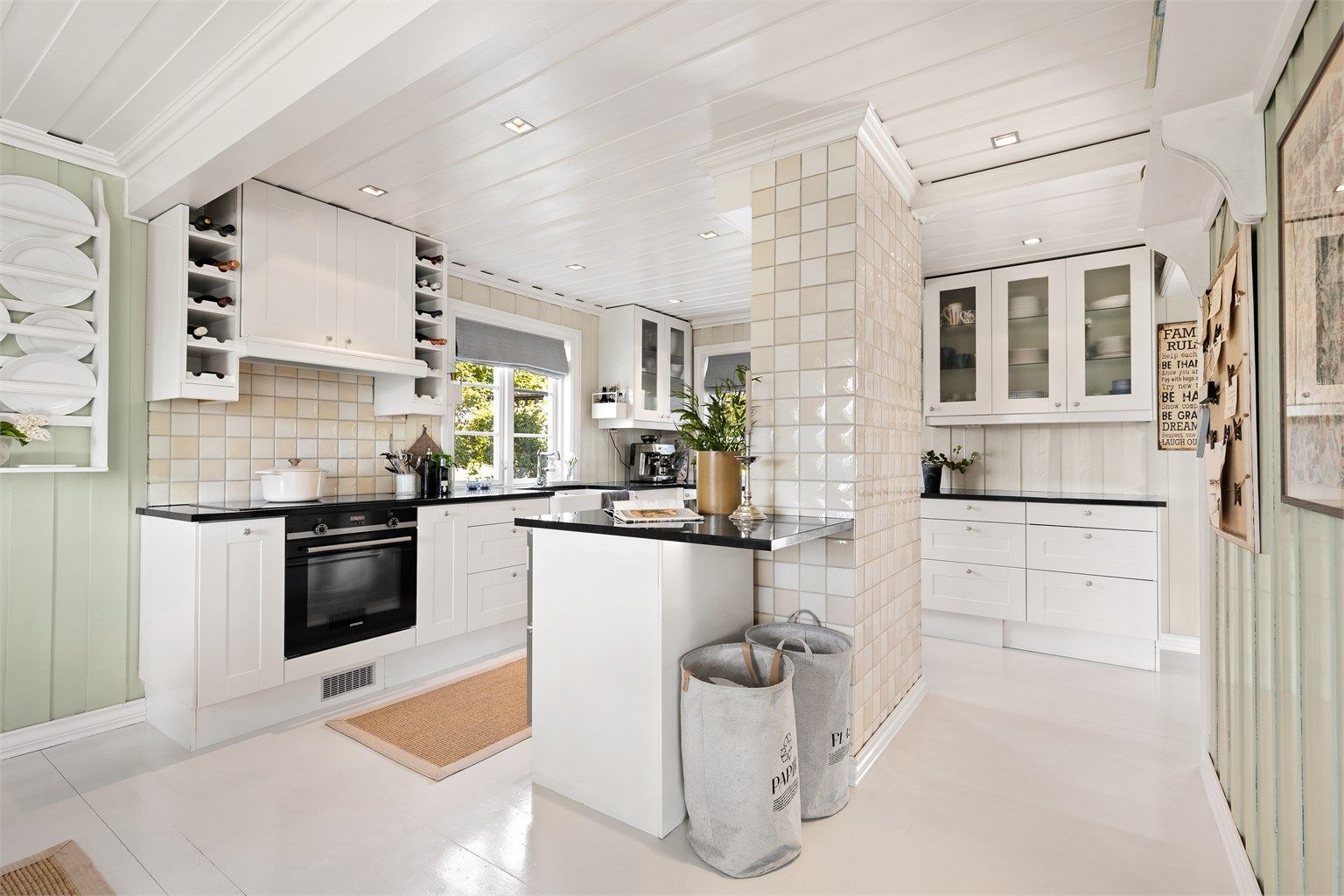 Kjøkken med gulvflate belagt med gulvbord av tre. Vegger med panel. Himling med panel. Nedsenket himling med downlights over deler av kjøkken.