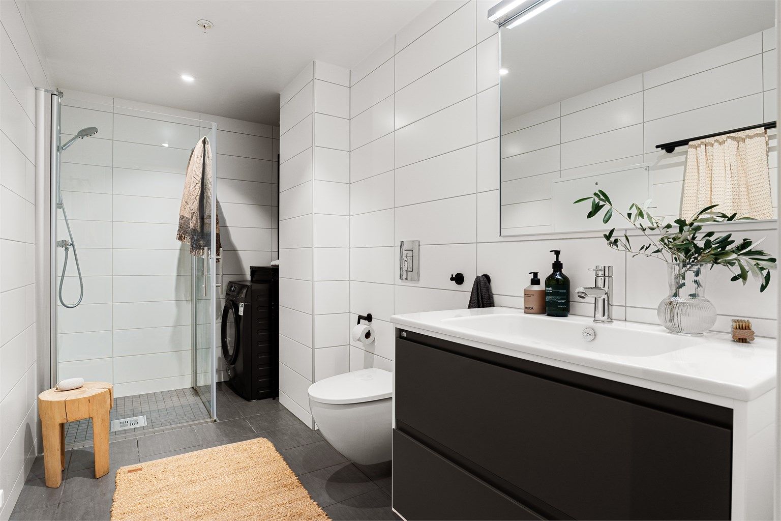 Badet fremstår moderne og stilrent med delikate flislagte vegger og gulv. Vannbåren gulvvarme sørger for god komfort, mens himling med malte plater og innfelte downlights gir behagelig belysning.