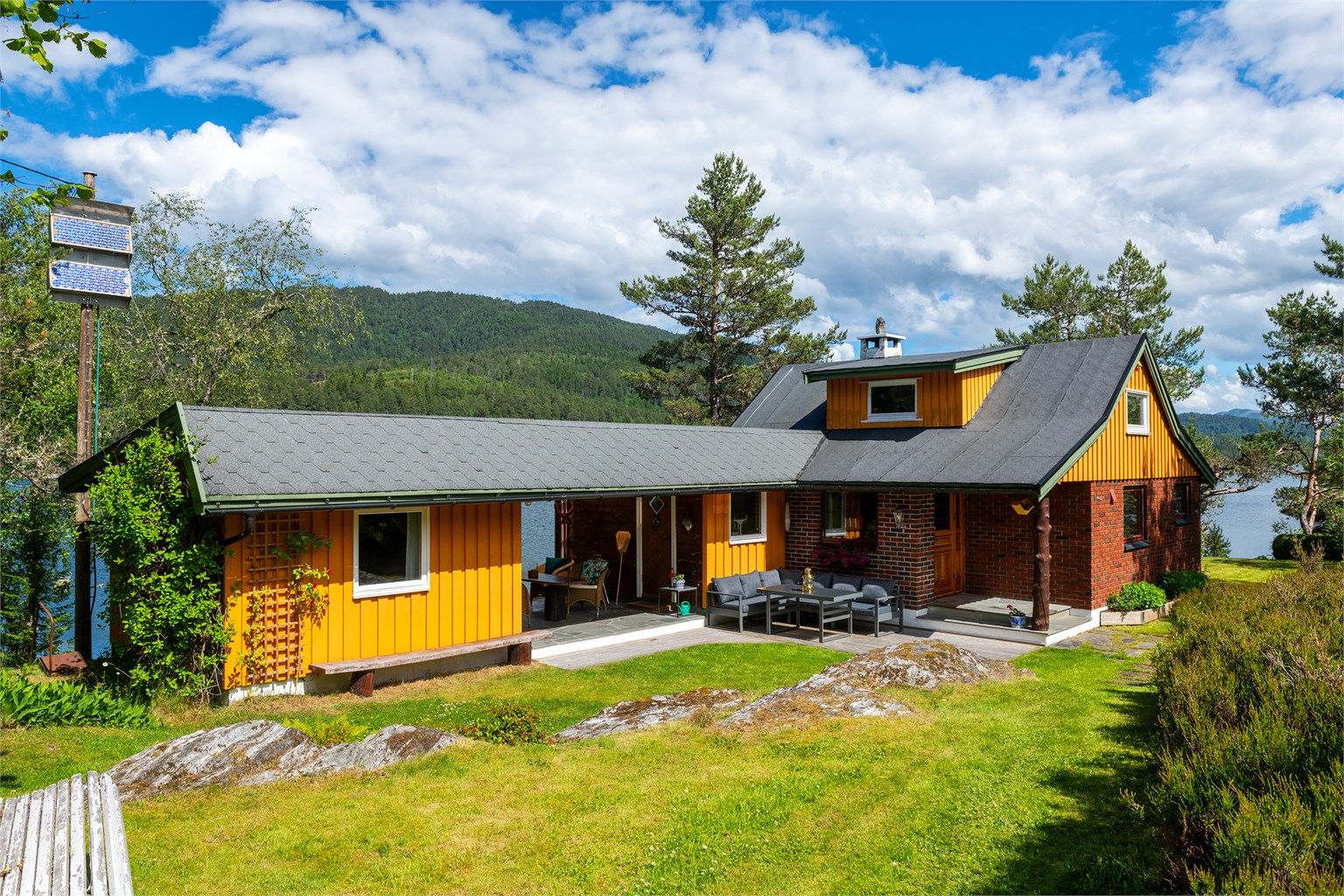 Fasade med markterrasse og hage og overbygget utestue