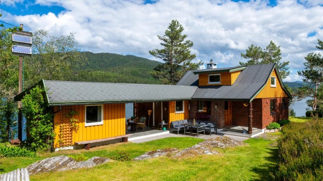 Fasade med markterrasse og hage og overbygget utestue