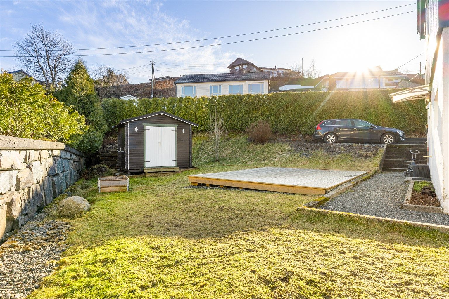 Bildet viser bla. biloppstillingsplass beregnet til utleieleiligheten hvor det også er montert egen el-bil lader. I tillegg er det satt opp en utebod.