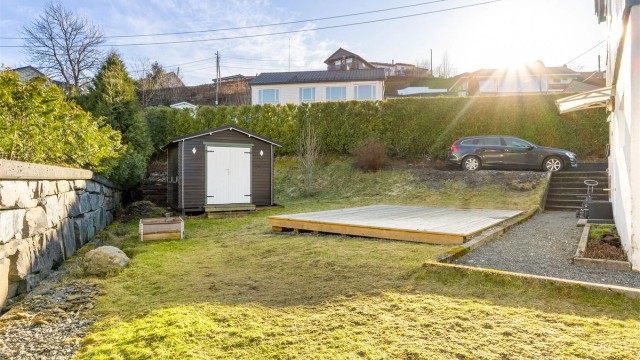 Bildet viser bla. biloppstillingsplass beregnet til utleieleiligheten hvor det også er montert egen el-bil lader. I tillegg er det satt opp en utebod.