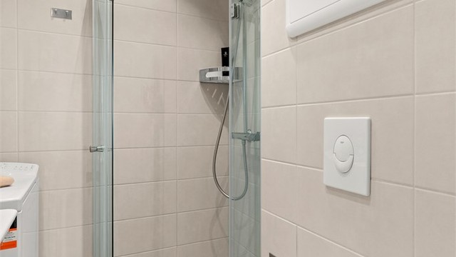 Lekkert baderom med vegghengt innredning, dusjhjørne med glassdører og opplegg for vaskemaskin.