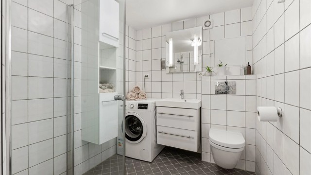 Flislagt bad med vegghengt toalett, dusjhjørne og opplegg for vaskemaskin.
