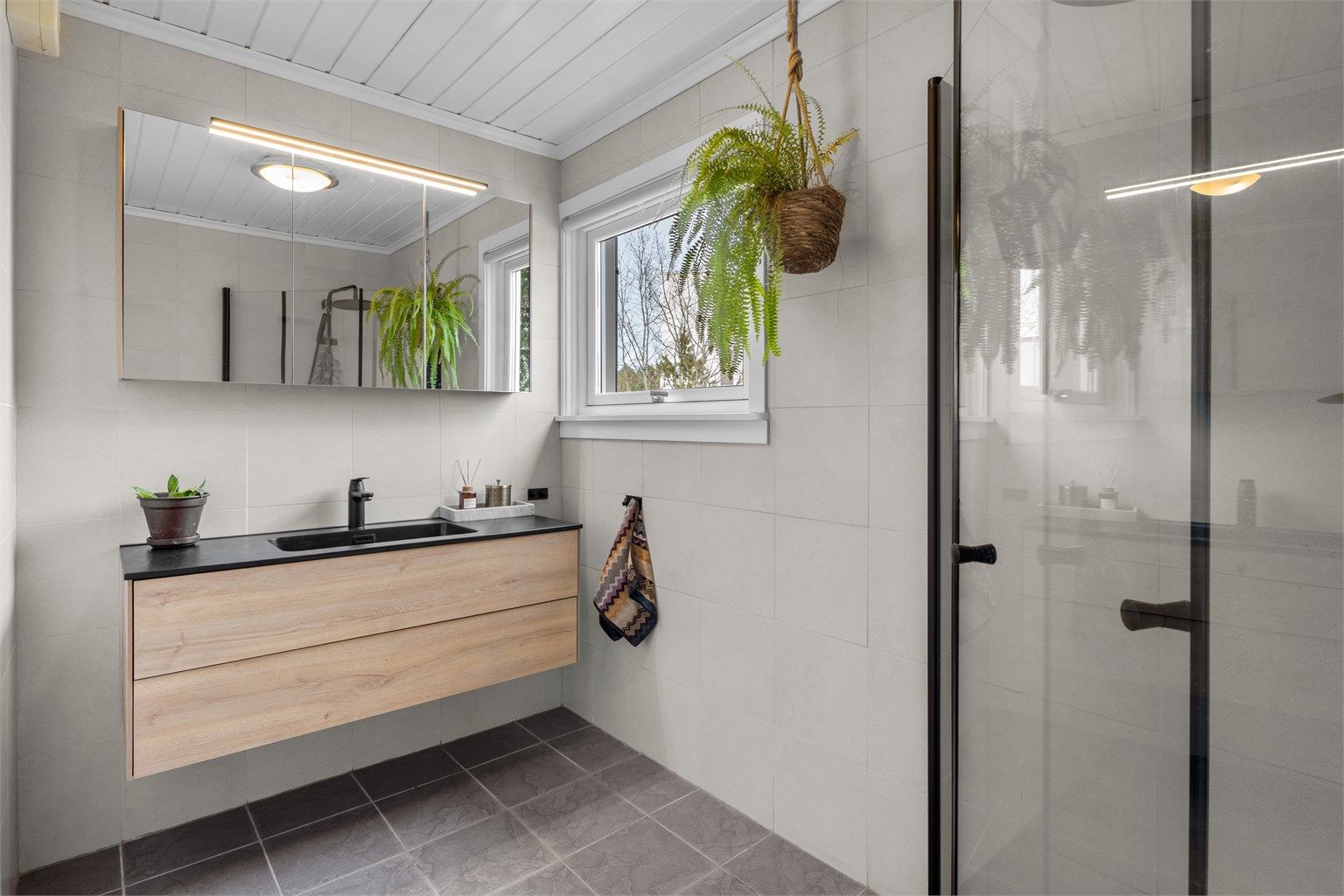 Moderne flislagt baderom som ble overflate oppusset med flis på flis i 2023, samt ny innredning og dusjhjørnet.