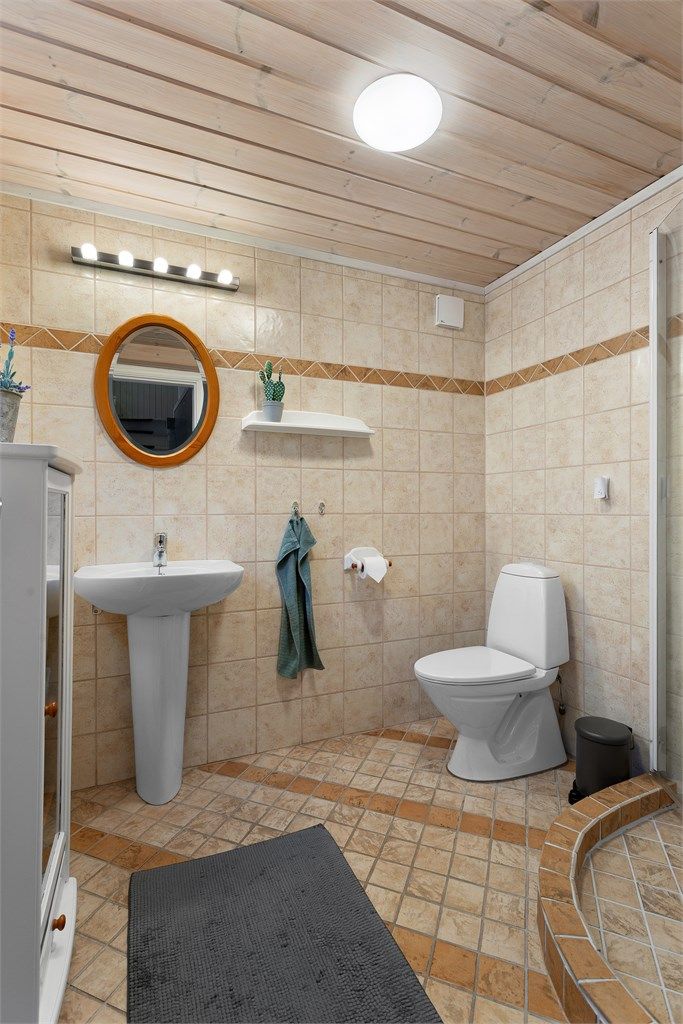 Flislagt bad med gulvvarme. Innredet med servant og speil på vegg med overlys. Dusjhjørne og gulvstående toalett.