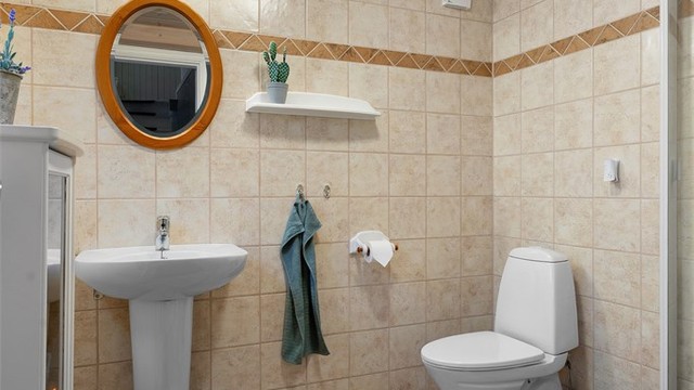 Flislagt bad med gulvvarme. Innredet med servant og speil på vegg med overlys. Dusjhjørne og gulvstående toalett.