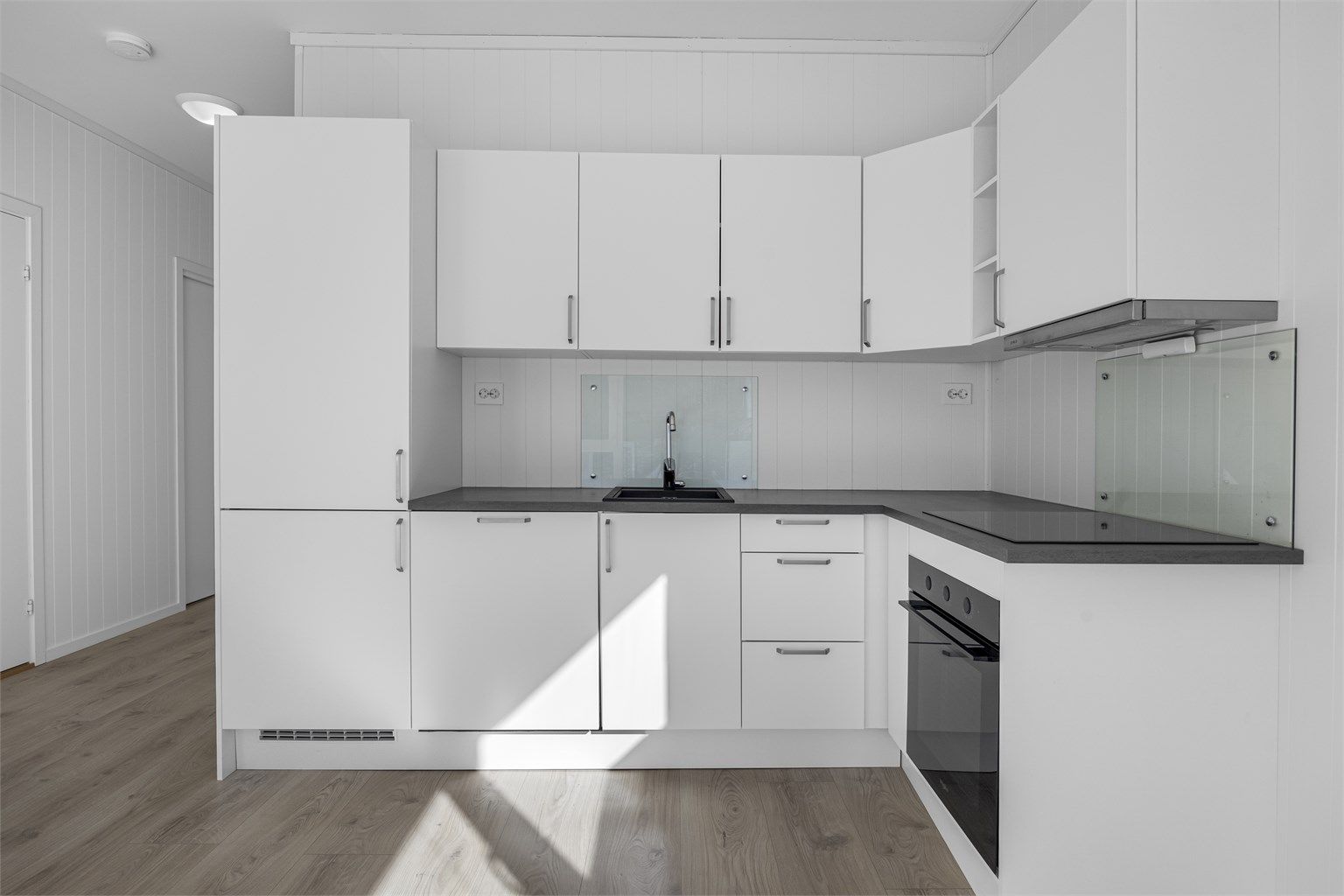 Kjøkkenet er en del av en åpen løsning og har innredning med glatte fronter og laminatbenkeplate.