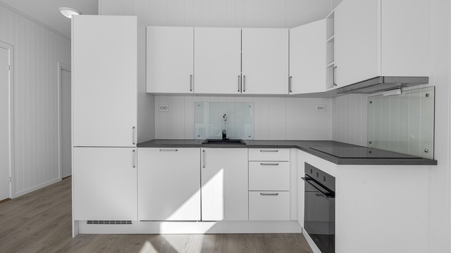 Kjøkkenet er en del av en åpen løsning og har innredning med glatte fronter og laminatbenkeplate.