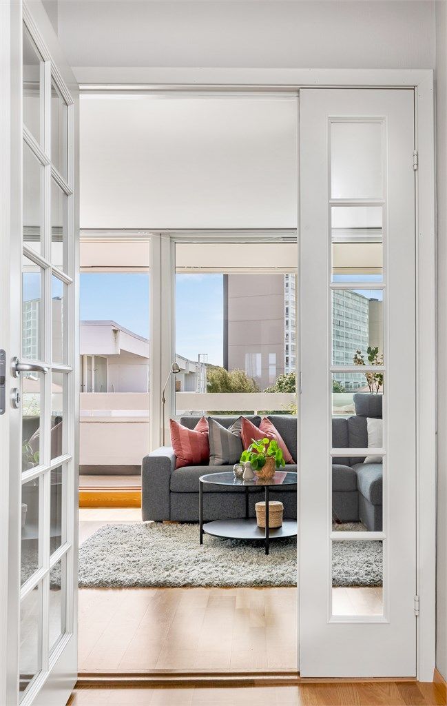 Lys og innbydende stue sett gjennom doble glassdører, med store vinduer som slipper inn rikelig med dagslys.