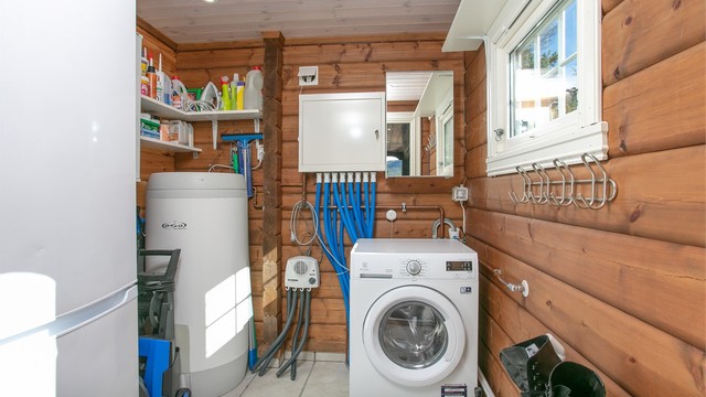 Praktisk vaskerom med flislagt gulv, opplegg for vaskemaskin og varmtvannsbereder.