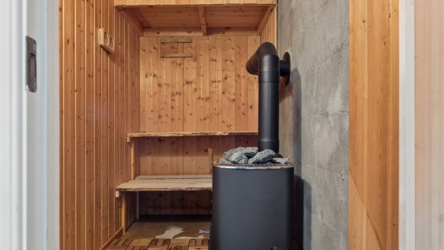 Badstue i underetasjen med trepanel og badstueovn for vedfyring.