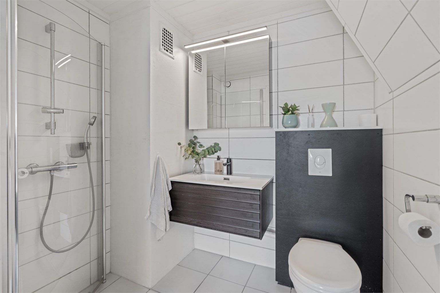 Badet har flislagte overflater, gulvvarme og vegghengt toalett.