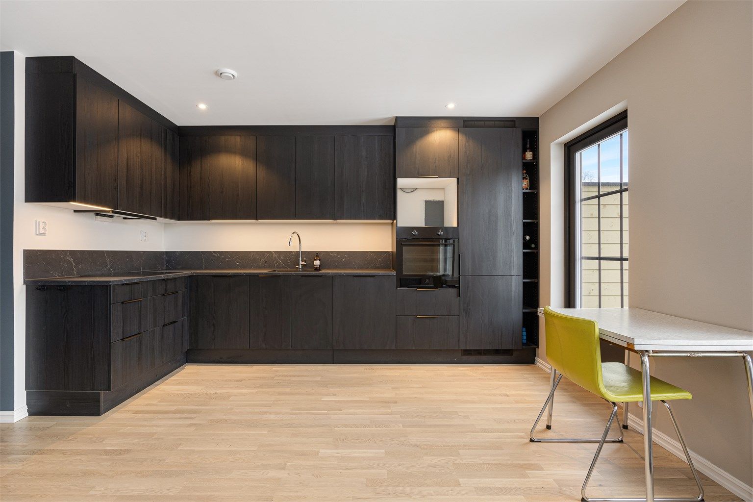 Stilrent og moderne kjøkken i L-form med sorte, glatte fronter og god skapplass.