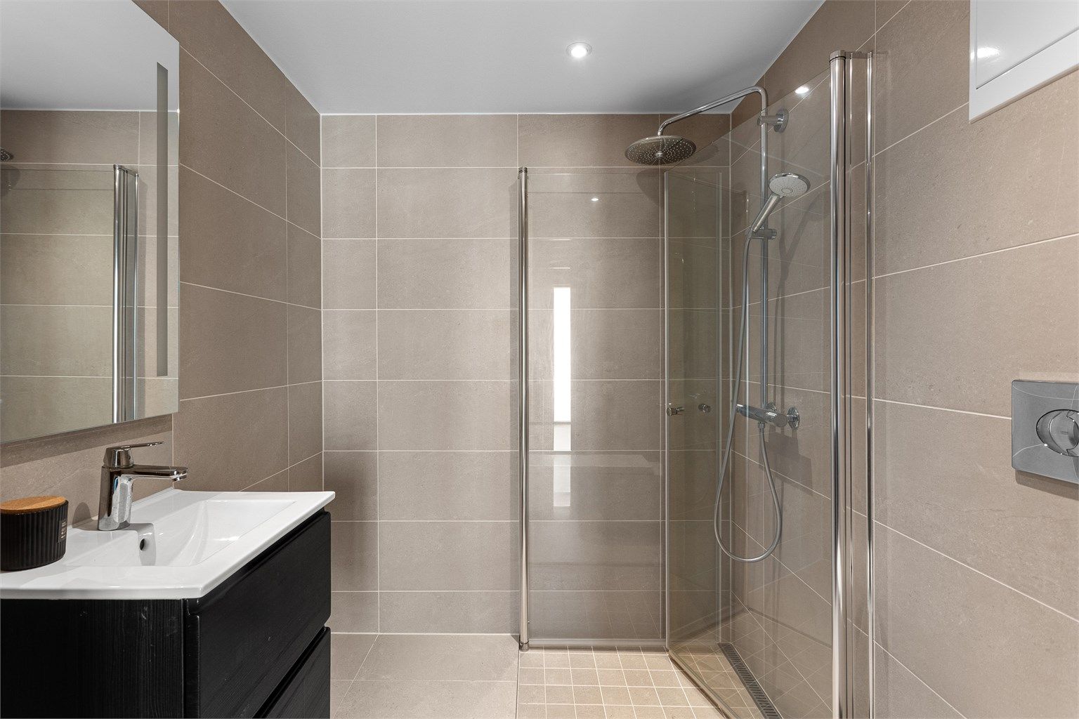 Leilighetens første baderom er innbydende med delikate fliser og vannbåren varme i gulv, samt downlights i himling. Perfekt gjestebad.