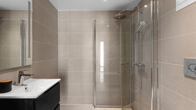 Leilighetens første baderom er innbydende med delikate fliser og vannbåren varme i gulv, samt downlights i himling. Perfekt gjestebad.