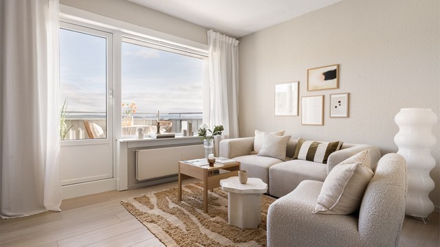 Stuen har god plass til både sofagruppe og spisebord, og store vindusflater slipper inn mye dagslys. Balkongdøren leder rett ut til utsikten, slik at uterommet føles som en naturlig forlengelse av stuen.