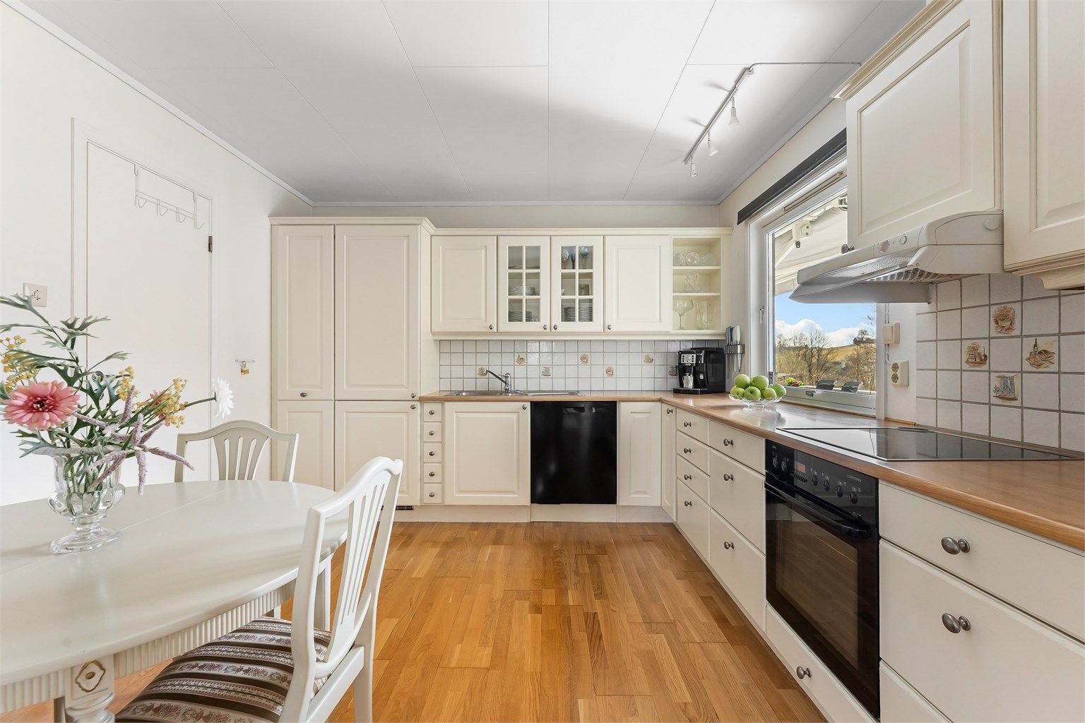 Pent kjøkken med profilerte fronter på skap og skuffer, benkeplate i laminat med nedfelt kjøkkenvask og veggfliser mellom benkeplate og overskap