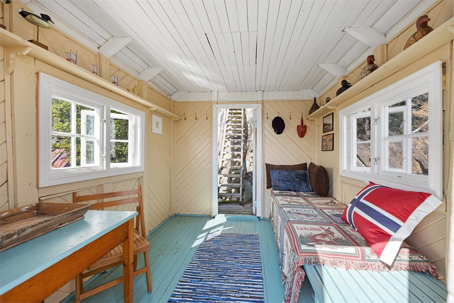 Badehuset er malt innvendig i lyse farger og har vinduer på to sider og dør direkte ut mot vannet.
