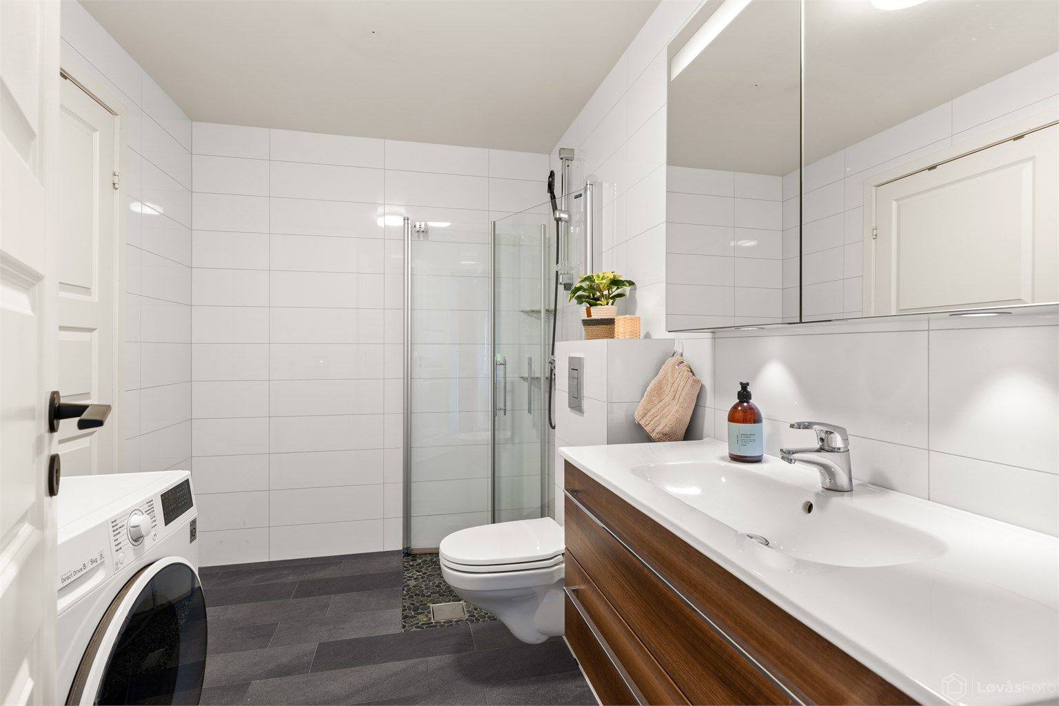 Romslig baderom med fliser på vegger og gulv samt gulvvarme. Direkte adkomst til praktisk innvendig bod for ekstra lagring.