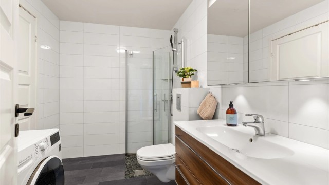 Romslig baderom med fliser på vegger og gulv samt gulvvarme. Direkte adkomst til praktisk innvendig bod for ekstra lagring.