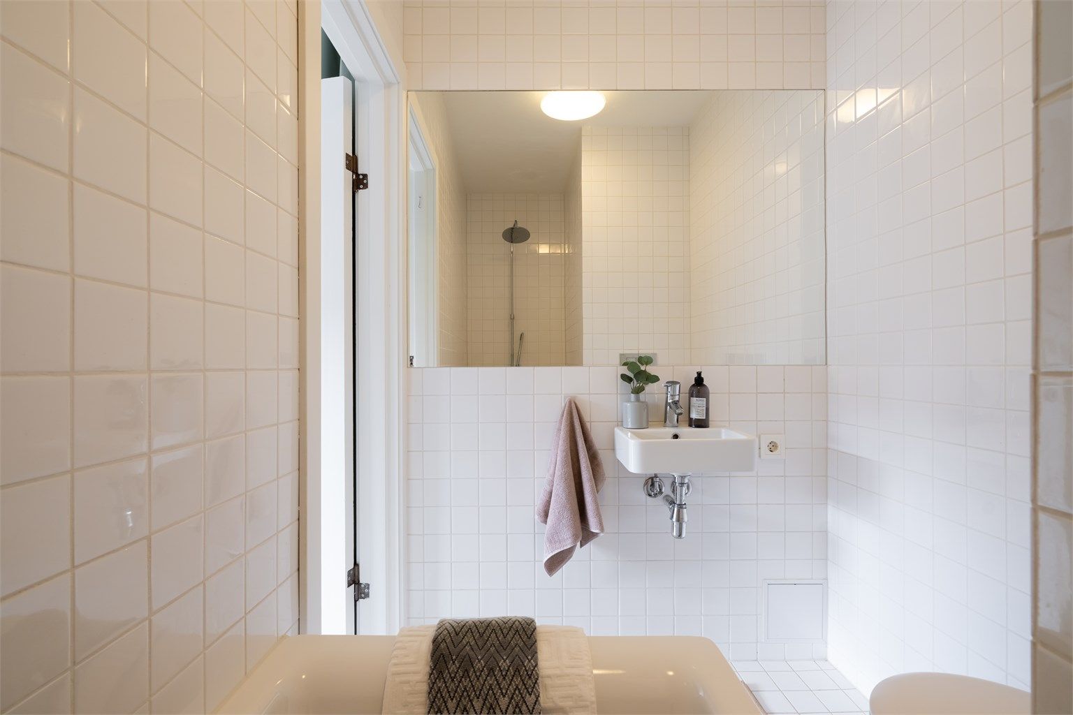 Badet er innredet med innmurt badekar, vegghengt toalett og servant. Stort speil over servanten og taklampe fra Arne Jacobsen - Eklipta.