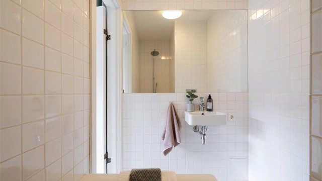 Badet er innredet med innmurt badekar, vegghengt toalett og servant. Stort speil over servanten og taklampe fra Arne Jacobsen - Eklipta.