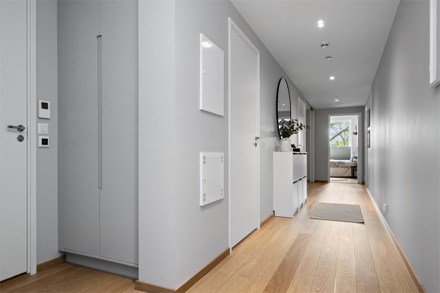 Langstrakt, flott entré med lysegrå, glatte vegger, downlights i himlingen og gyllen, enstavs parkett på gulv med vannbåren gulvvarme.