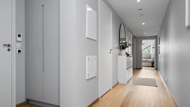 Langstrakt, flott entré med lysegrå, glatte vegger, downlights i himlingen og gyllen, enstavs parkett på gulv med vannbåren gulvvarme.