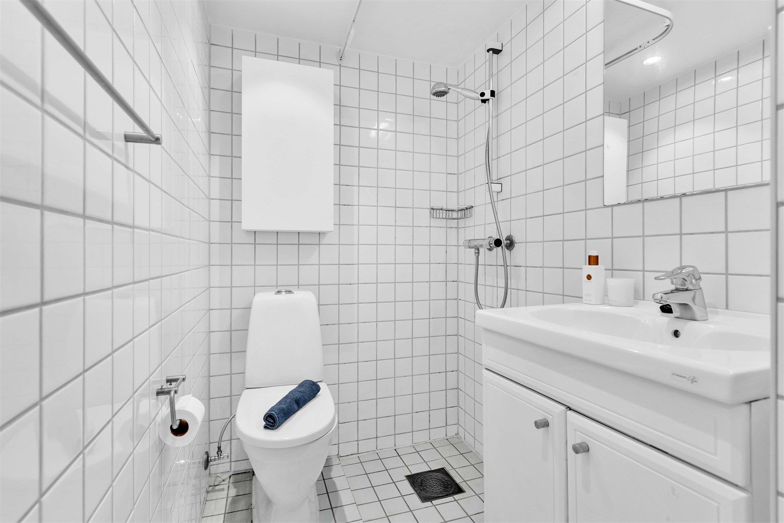 Lyst flislagt bad med vegghengt innredning og skapplass for oppbevaring