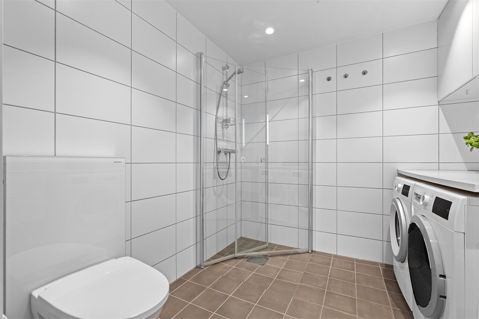 Romslig dusjsone med glassdører og praktisk innredning som gir badet en funksjonell utforming.
