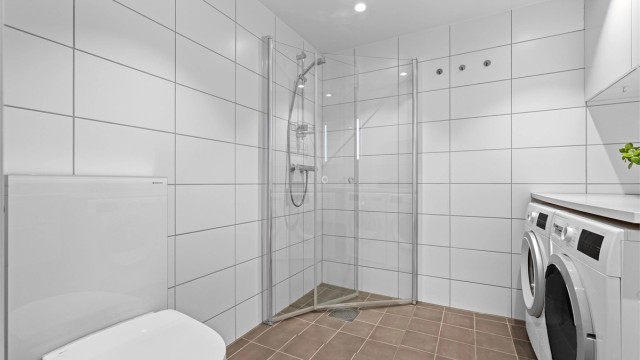 Romslig dusjsone med glassdører og praktisk innredning som gir badet en funksjonell utforming.