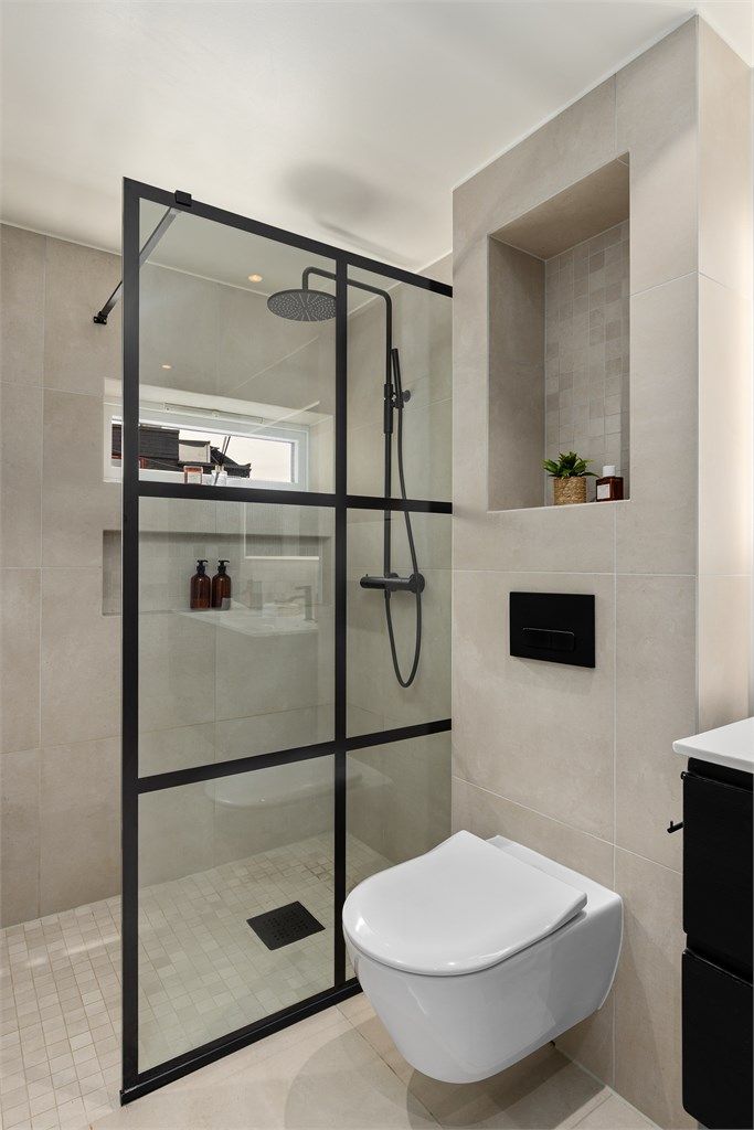 Stor dusjnisje med regnfallsdusj og integrert hylle. De sorte detaljene er beholdt gjennom leiligheten