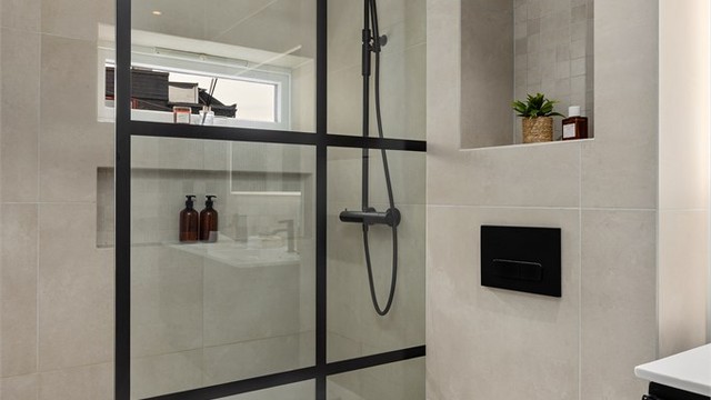 Stor dusjnisje med regnfallsdusj og integrert hylle. De sorte detaljene er beholdt gjennom leiligheten