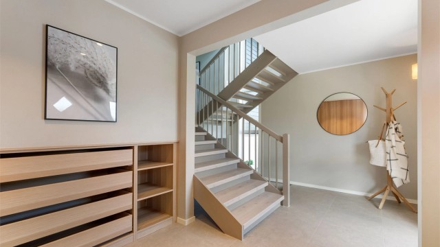 Gjennomført og innbydende entré med store fliser på gulv med behagelig gulvvarme, og et elegant trappeløp.