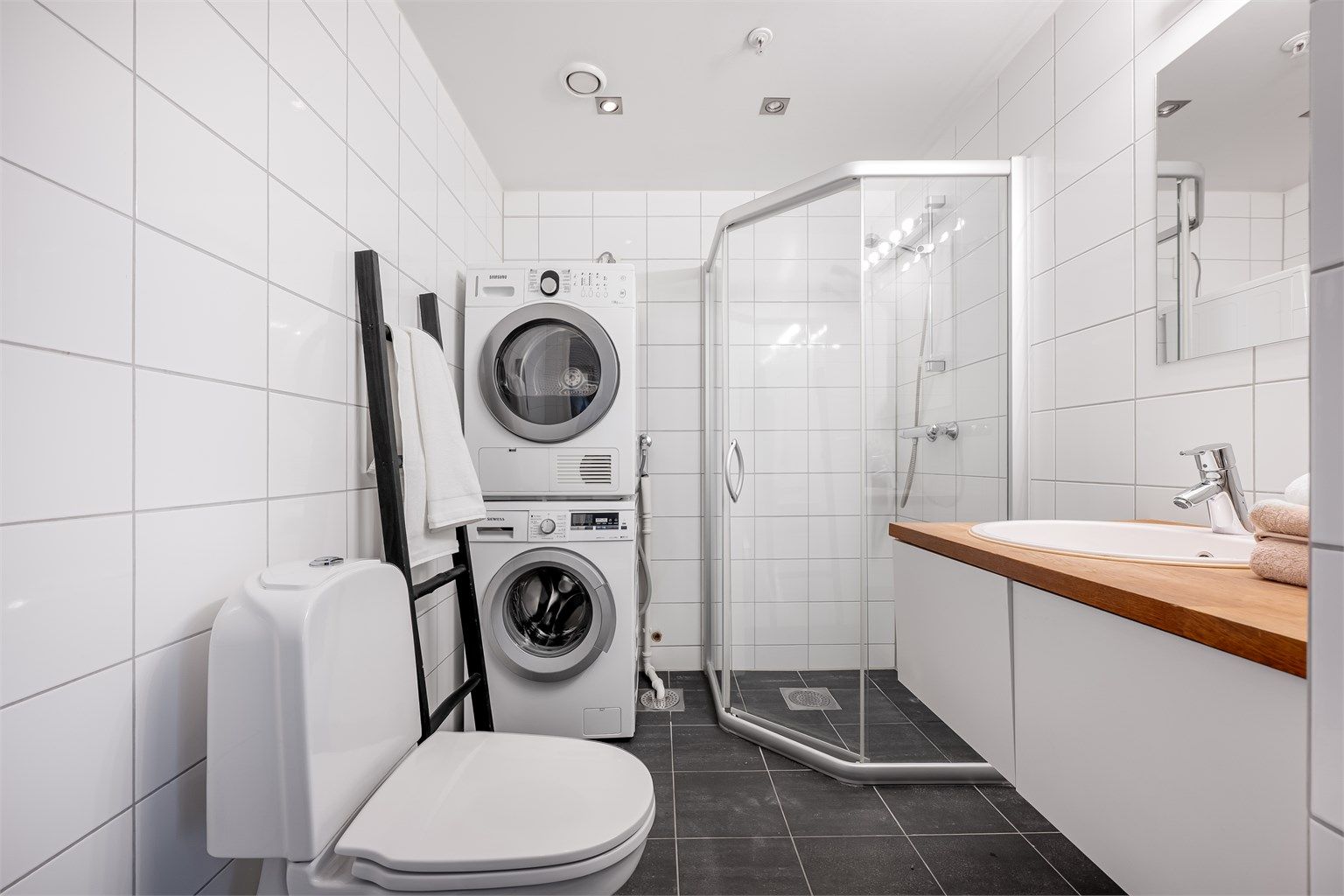 Fint helfliset bad av godt størrelse med varme i gulv. Det er dusjhjørne, toalett og servant med oppbevaringsplass i skuffer. Stort speil på vegg. Opplegg for vaskemaskin samt plass til tørketrommel om man skulle ønske det. Et fint og stilrent baderom. 