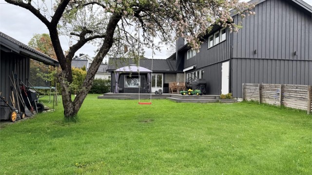 Pent opparbeidet hage med stor og flat gressplen og diverse beplantninger