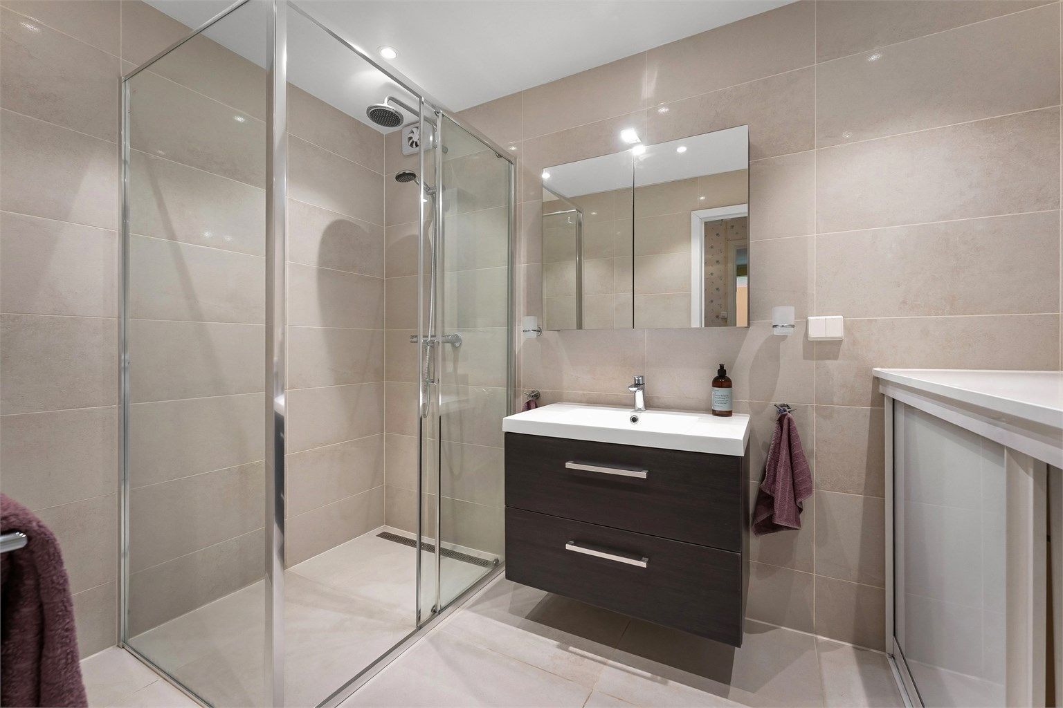 Badet i første etasje er flislagt og utstyrt med gulvvarme, downlights og dusjhjørne med regndusj.
